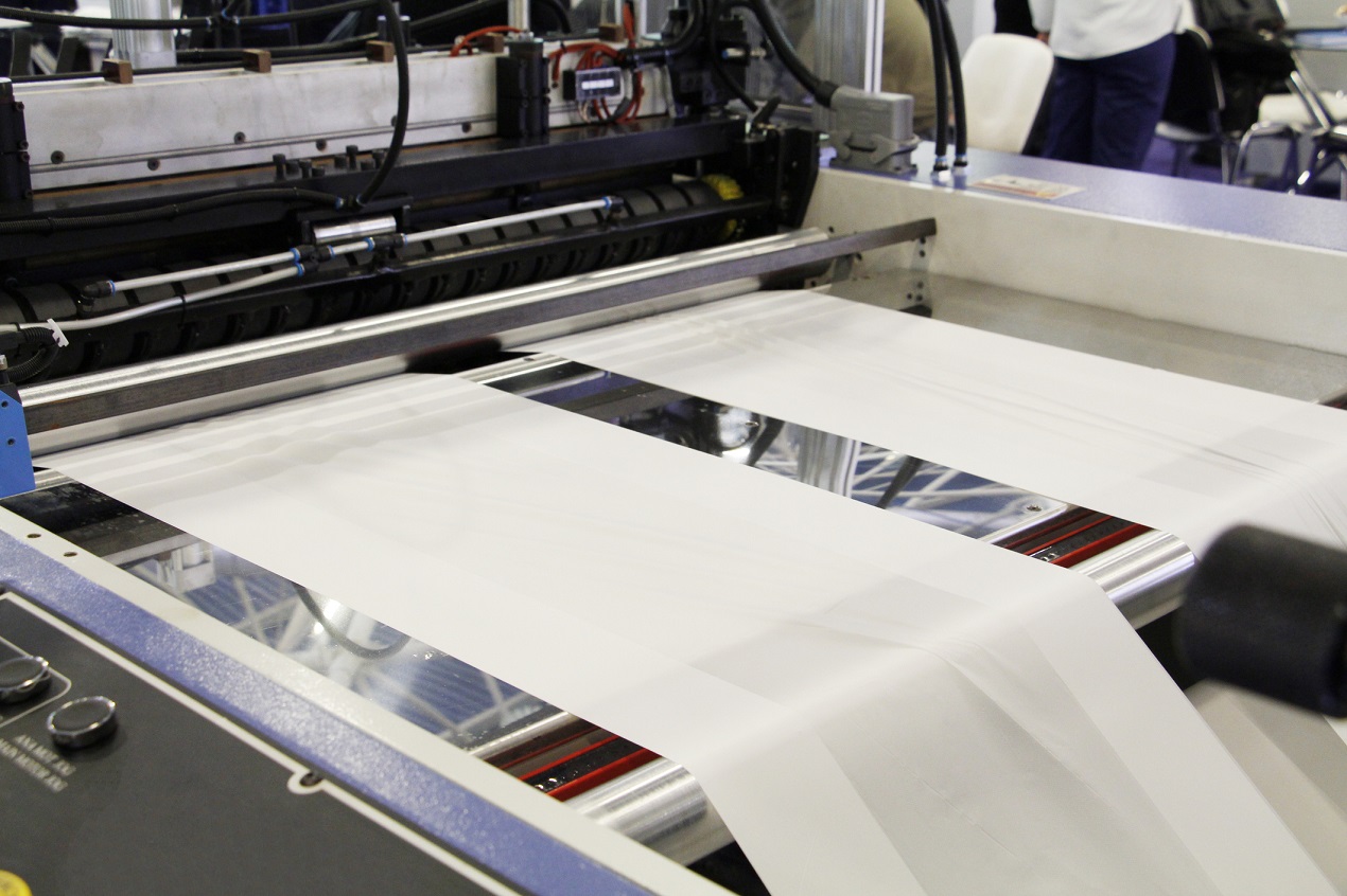 A fragment of a machine for the production of plastic bags. The production of plastic bags at the factory. The shafts are spinning. Cellophane moves between the shafts.